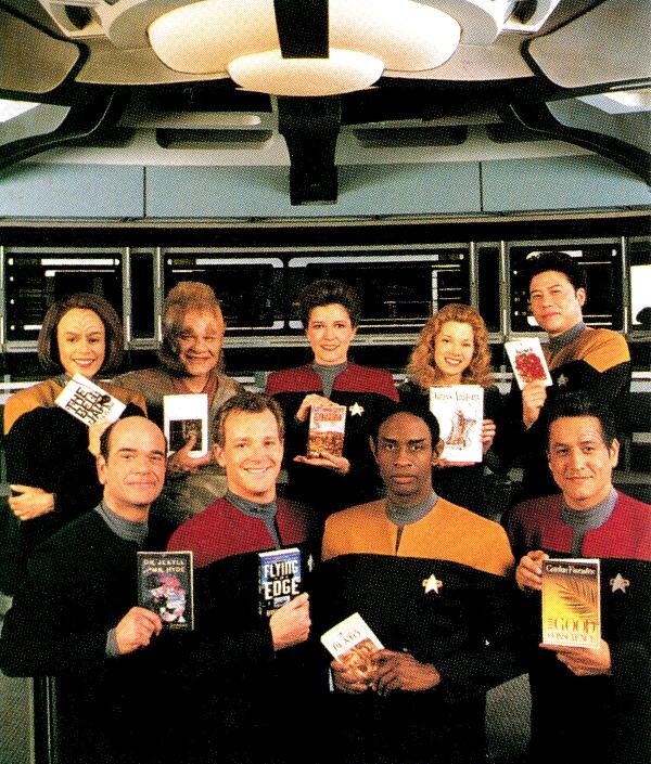 The senior crew of B'Elanna, Neelix, Kathryn, Kes, Harry, The Doctor, Tom, Tuvok and Chakotay on the bridge holding their favourite books.