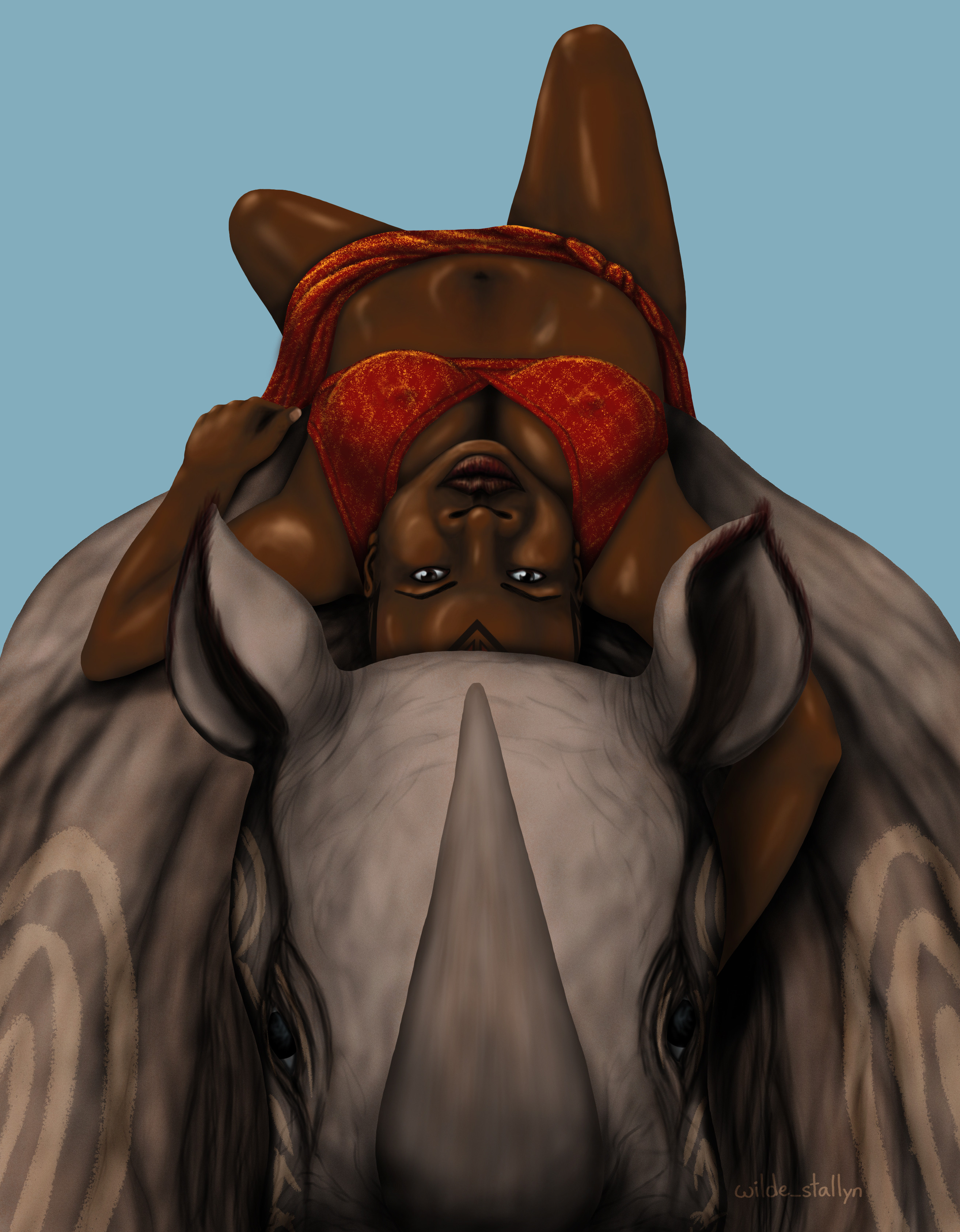 Okoye lying on her back on top of a war rhino, seen from in front so that she is looking at he viewer upside down. She is wearing a red and gold bikini top and wrap skirt
