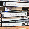 a stack of black recorded VHS tapes with white labels that have non readable text on them