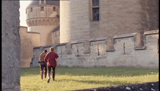 a shot of Arthur chasing Merlin in the sunshine on the grounds outside of the castle.