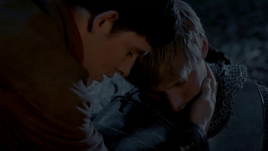 a somber picture of Merlin with his forehead pressed against Arthurs as he checks Arthurs pulse