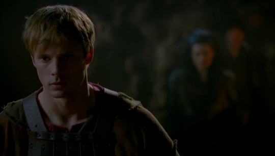 a picture of Arthur looking toward the ground with a shocked sad expression on his face and in the blurry background is Morgana getting ready to attack
