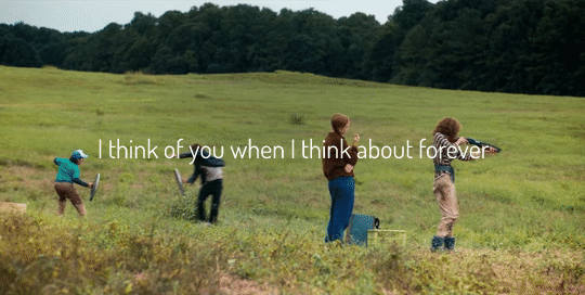 gif of Eddie and Dustin play fighting in the field with the trashcan shields you can also see Nancy practicing shooting and Lucas practicing with his spear - the text reads I think of you when I think about forever.