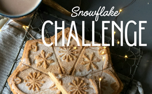 Snowflake Challenge: A flatlay of a snowflake shaped shortbread cake, a mug with coffee, and a string of holiday lights on top of a rustic napkin.