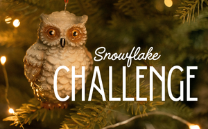 Snowflake Challenge: A close up shot of an owl ornament hanging amidst pine boughs..