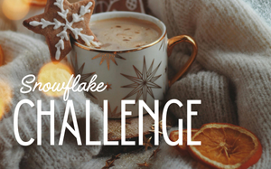 Snowflake Challenge: A mug of coffee or hot chocolate with a snowflake shaped gingerbread cookie perched on the rim sits nestled amidst a softly bunched blanket. A few dried orange slices sit next to it.