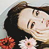 an asian woman in a bathtub filled with water, her head submerged except for her face. flowers float in the water near her face